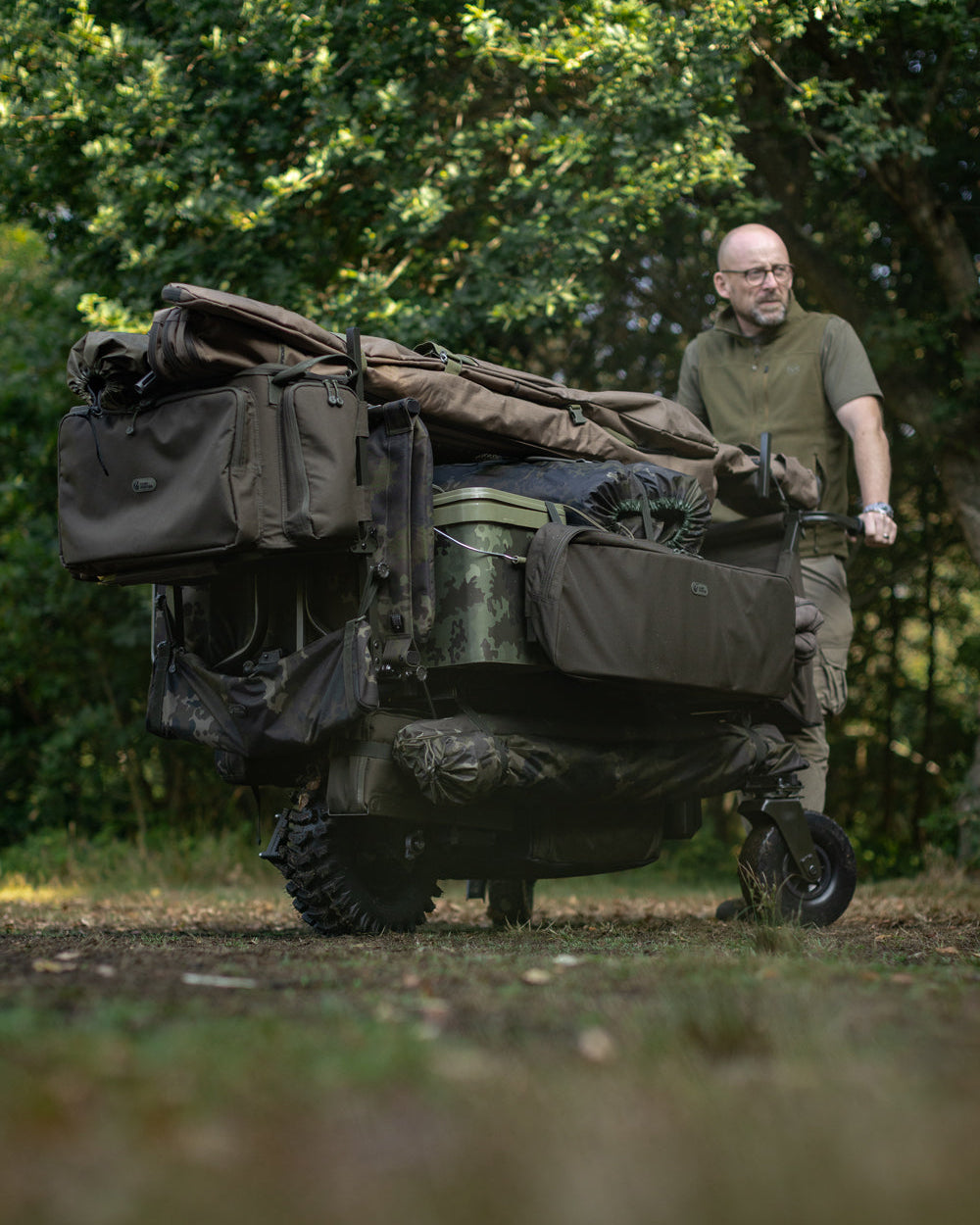 Man pushing a large green cart with camping gear through a forest